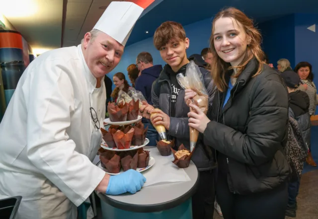 1 male and 1 female student icing cakes with male lecturer