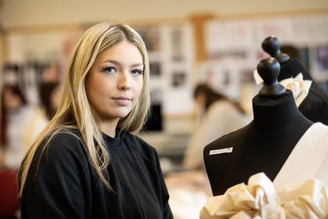 A fashion student is standing in class next to a mannequin