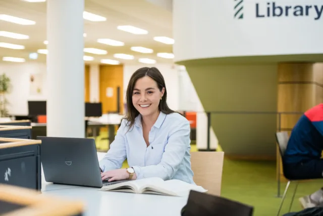 Students are smiling whilst sitting around a desk in the Mayo library