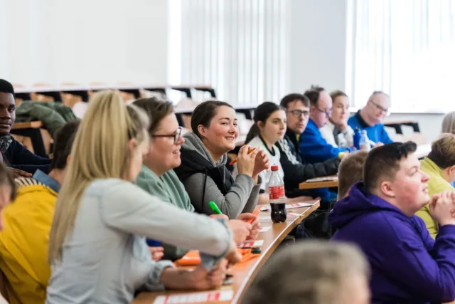 A group of students are smiling whilst in a lecture theatre