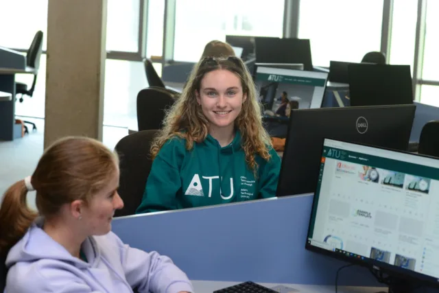 A computing student in an ATU hoodie is working in a computer lab