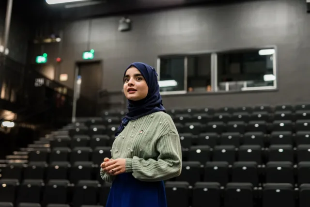 A student stands in front of an empty lecture theatre