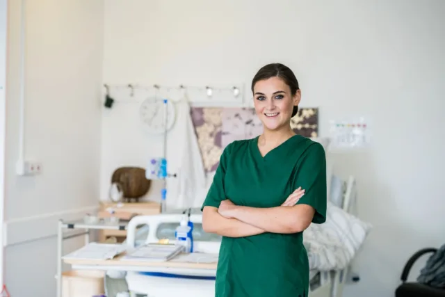 A nursing student stands smiling in a hospital ward on the St Angelas campus