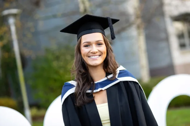 Female Graduate poses in graduation gown and cap