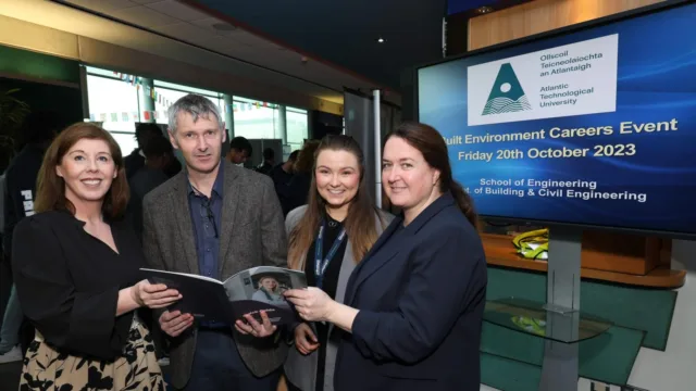 Four people at a careers fair, holding an ATU brochure and looking up and smiling at the camera.