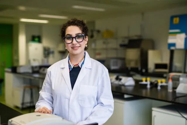 Female student in lab coat stands in ATU science lab.