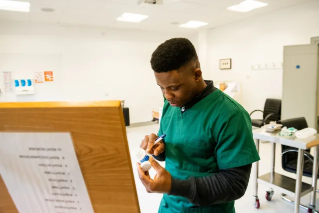 Male nursing student in green scrubs examines a medicine bottle