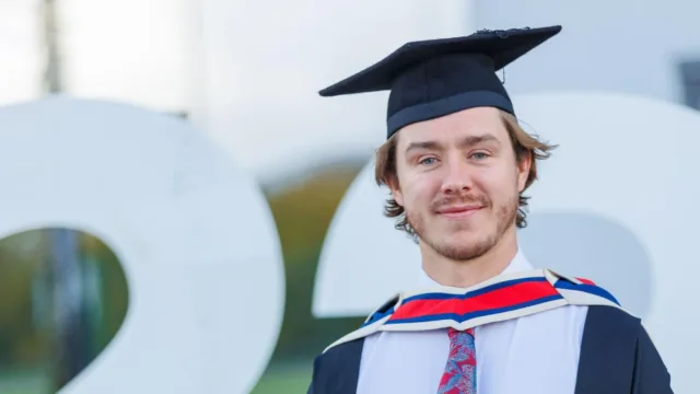 ATU graduate smiles for the camera, wearing a cap and gown