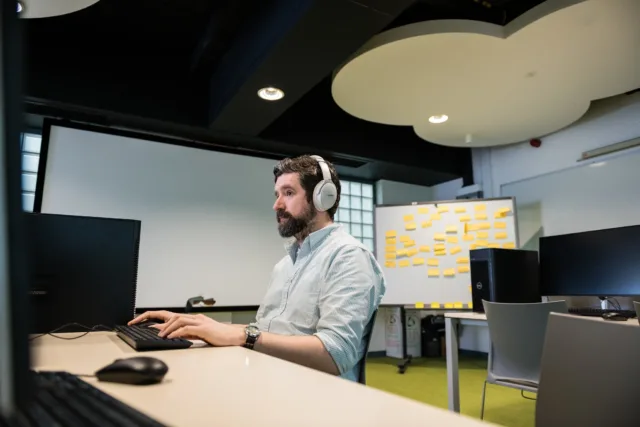 Student in creative computer lab wearing headphones and looking at computer