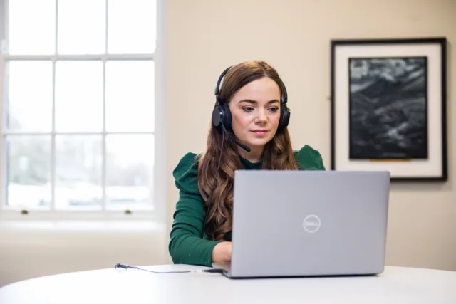 Female student in green top wearing headphones while working at a laptop