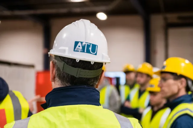 Back of student's head, wearing a white hard hat with a blue sticker that reads "ATU"