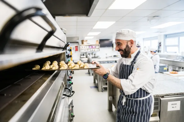 Male student from the Galway International Hotel School in apron and white uniform putting pastries in the oven