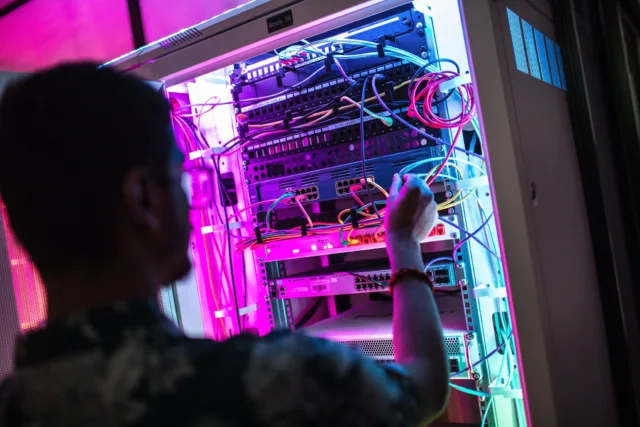 Student looks at wiring in data storage hardware lit up by multi-coloured LED lights