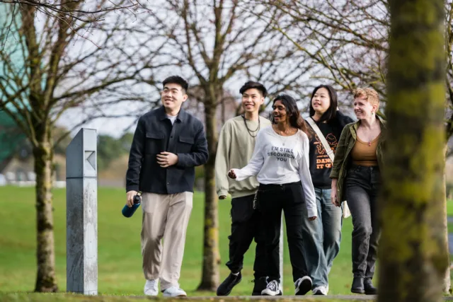 International students, two boys and three girls, walking through the Galway City campus grounds.