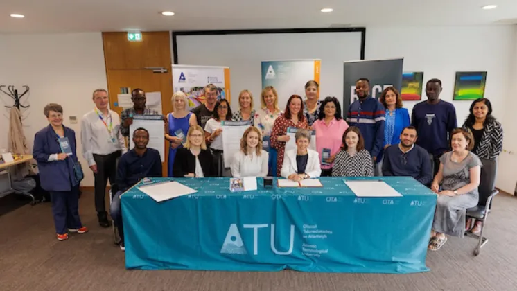 A large group pictured together at the signing of the HEA’s Race Equality Anti-Racism Principles. People are seated at a table with ATU branding, signing the document, while others are gathered around, smiling towards the camera.