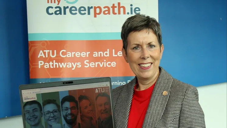 ATU President Dr. Orla Flynn holds up a laptop, smiling for the camera