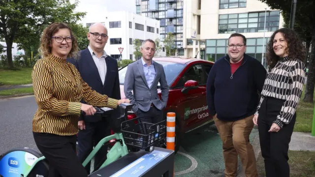 A group of people pictured in front of a red electric car, with one woman holding the handlebars of an e-bike.