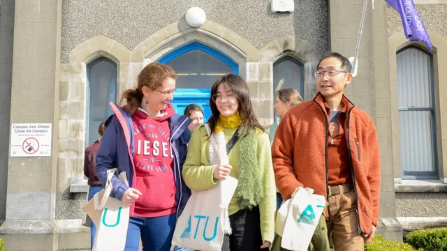 A student smiling as she leaves the campus alongside her mum and dad, with all three holding ATU tote bags.