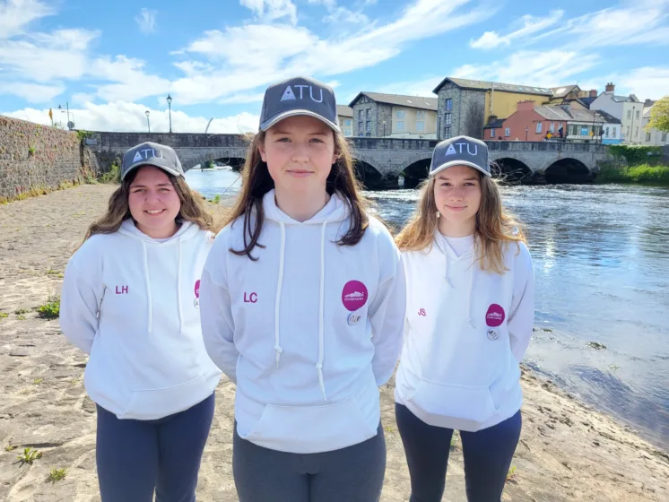 Three members of an all-female Formula 1 in Schools team to reach the world finals, pose beside the river in their town wearing ATU caps.