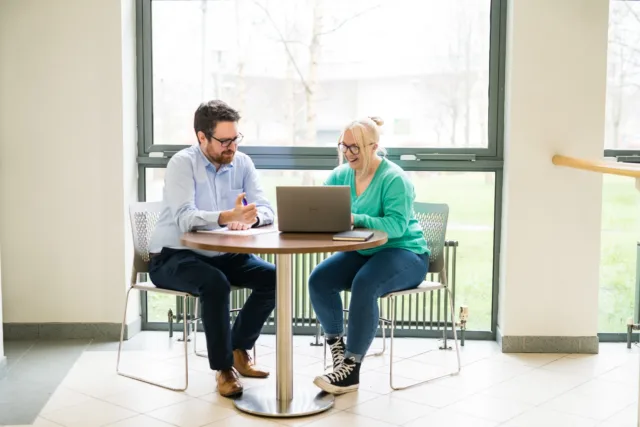 Male and Female student sitting at a table chatting and looking at a laptop together