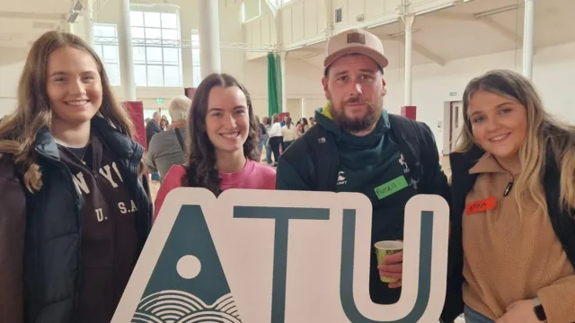 Four students stand together, holding up an ATU sign for the photo.