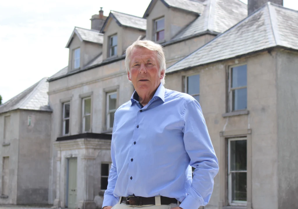 Veterinary surgeon Donal Connolly, one of the three founding members of the Aleen Cust Memorial Society, standing in front of Cordangan Manor, the birthplace of Aleen Cust, with the manor house in the background.