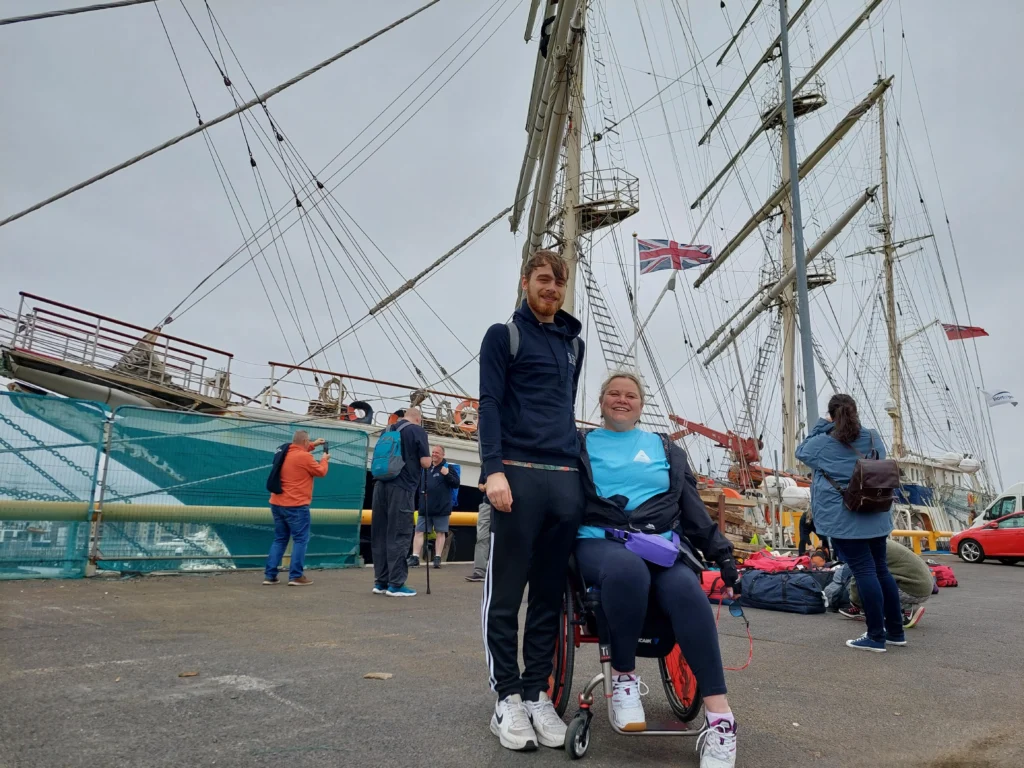 Victoria Matthews, a wheelchair user and ATU Sligo Sport with Business student, with her son Luca, an ATU student, smiling for the camera on the pier with the ship in the background.