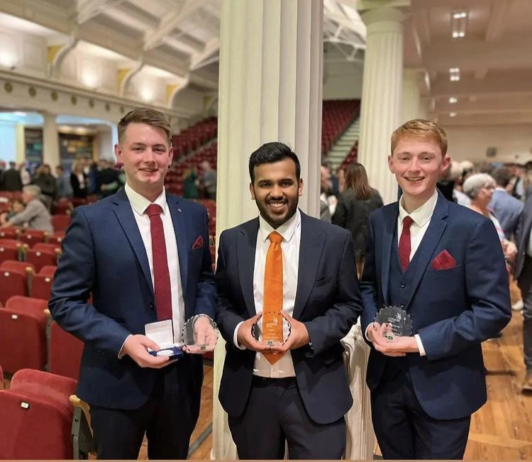 Three ATU hotel management students holding their trophies, smiling for the camera.