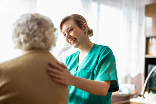 Nurse in green scrubs has her hand gently on the back of an older lady