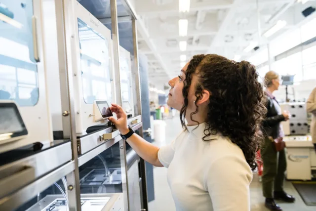 Gabriella, an international student, looks through the glass of a 3D printer