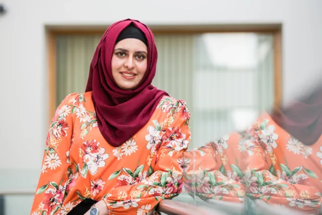 Female student in orange top and red hijab poses in a corridor in the ATU Galway City, Dublin Road campus