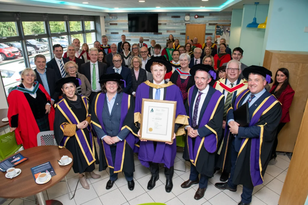 Joseph Kennedy stands with ATU staff crowd holding honorary Doctorate