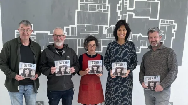 3 men and 2 women stand in a line holding book called Stamp