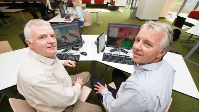 Two students at computer face towards camera