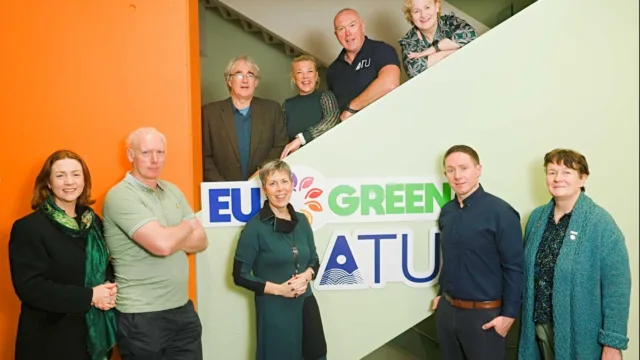 ATU team members involved in the EU Green project pose for a photo, with some standing on a staircase and others in front of the staircase, where ATU and EU Green signs are displayed.