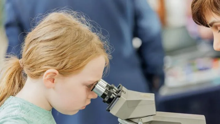 Child with red hair looks through microscope