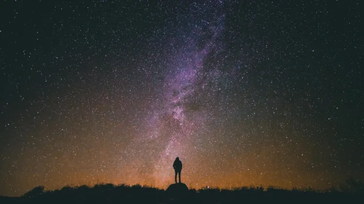 persson standing on a rock in the dark looking at a sky filled with stars