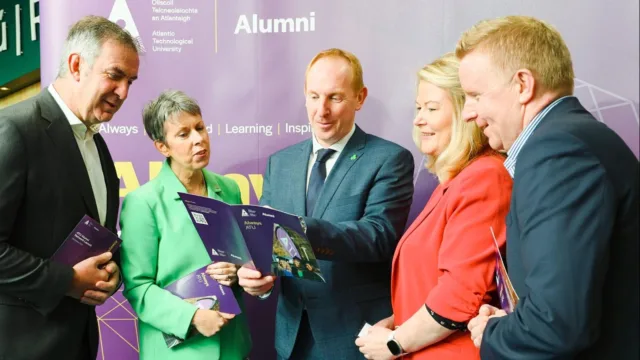 A group of people engaged in looking at the contents of an open brochure, held by the man in the centre.