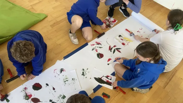 A shot from above of children painting, with their brushes and artwork visible on the table.