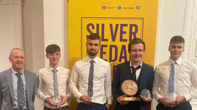 At WorldSkills, four apprentices stand with their ATU lecturer, all holding trophies, with one apprentice holding two.