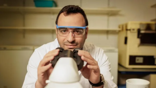 Scientist stares holds microscope and looks at the camera