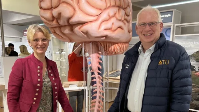 Two ATU staff members smile for a photo in front of a large brain sculpture, part of Science Week celebrations.