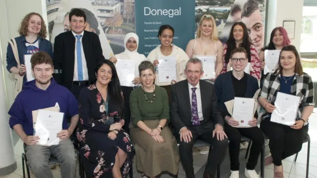 Two rows of students with staff members. One row is standing, and the other row is sitting in front, all smiling at the camera. The students are holding up certificates.