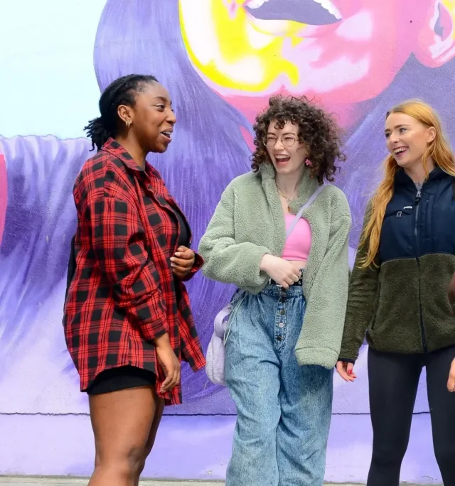 Four female students chatting in front of colourful mural of woman.