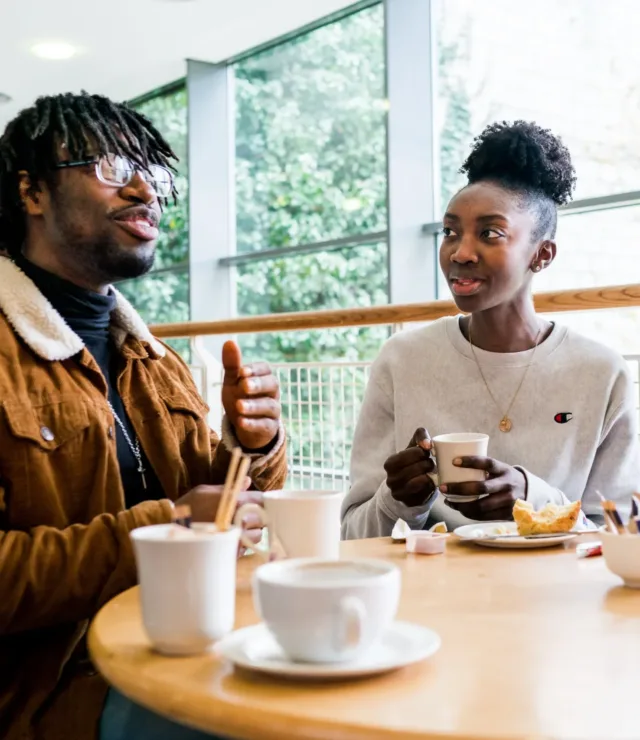 Three students sitting around table chatting and drinking coffee