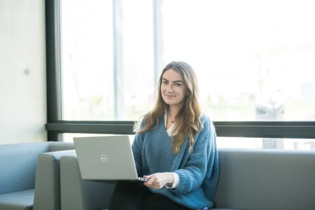 Woman sitting holding a laptop wearing a blue jumper