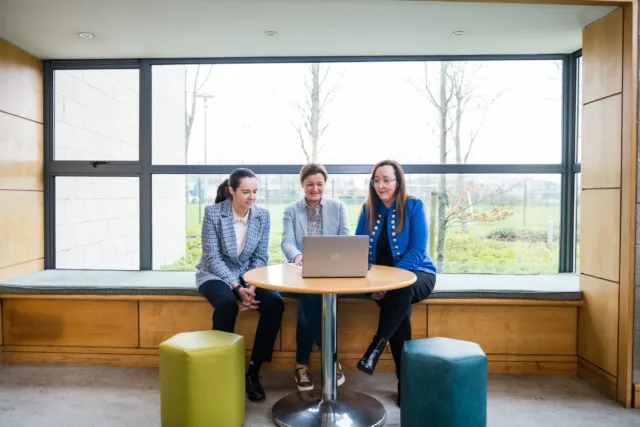 Three people sitting at a laptop