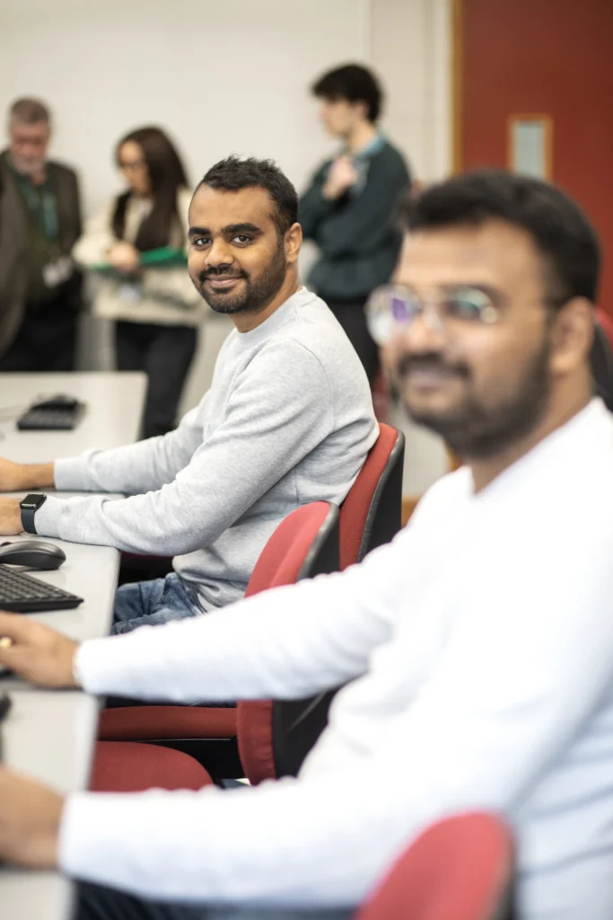 Two male international students sit at computers in computer lab