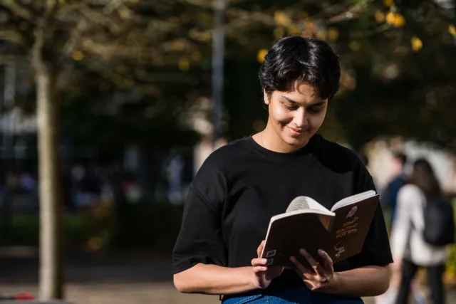 International student reads a book outdoors