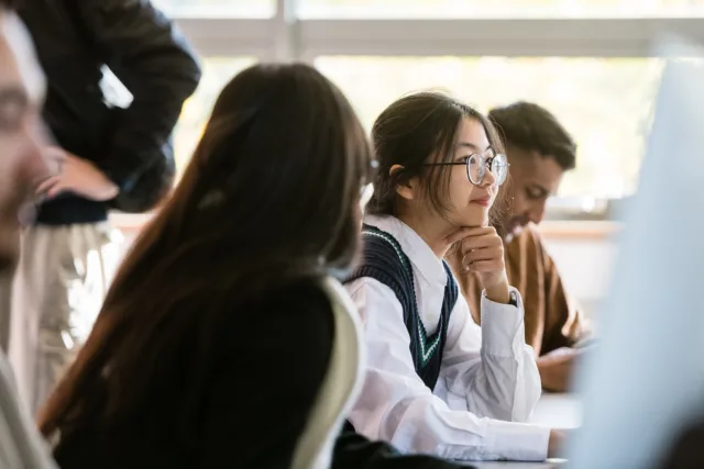 Female international student with glasses gazes into computer screen in a computer lab